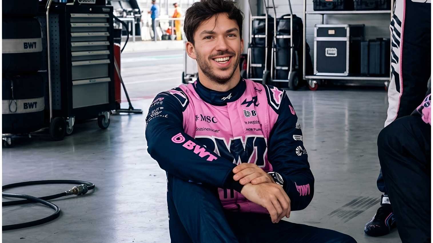 Pierre Gasly wearing pink and navy BWT Alpine F1 Team race suit, smiling while seated in the garage during the 2026 season