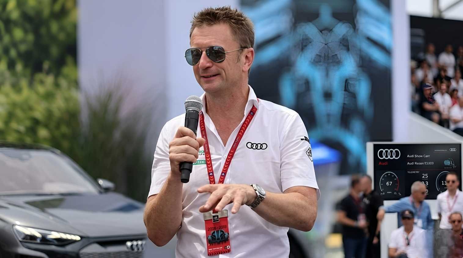 Allan McNish speaking at Audi Sport event wearing team shirt and sunglasses, appointed Audi F1 Racing Director 2026