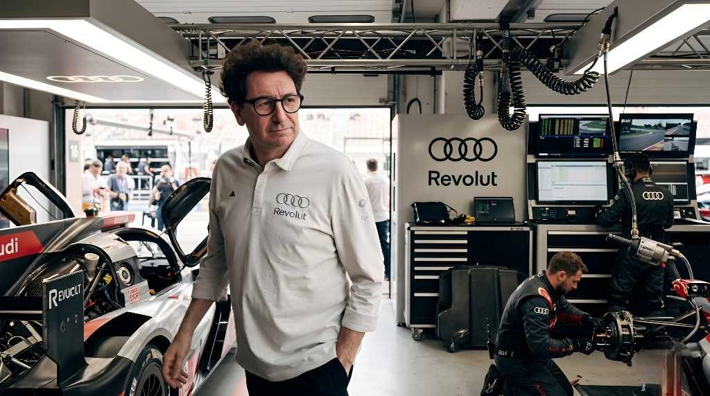 Audi F1 Team Principal Mattia Binotto wearing Audi Revolut polo standing in race garage next to a motorsport prototype car