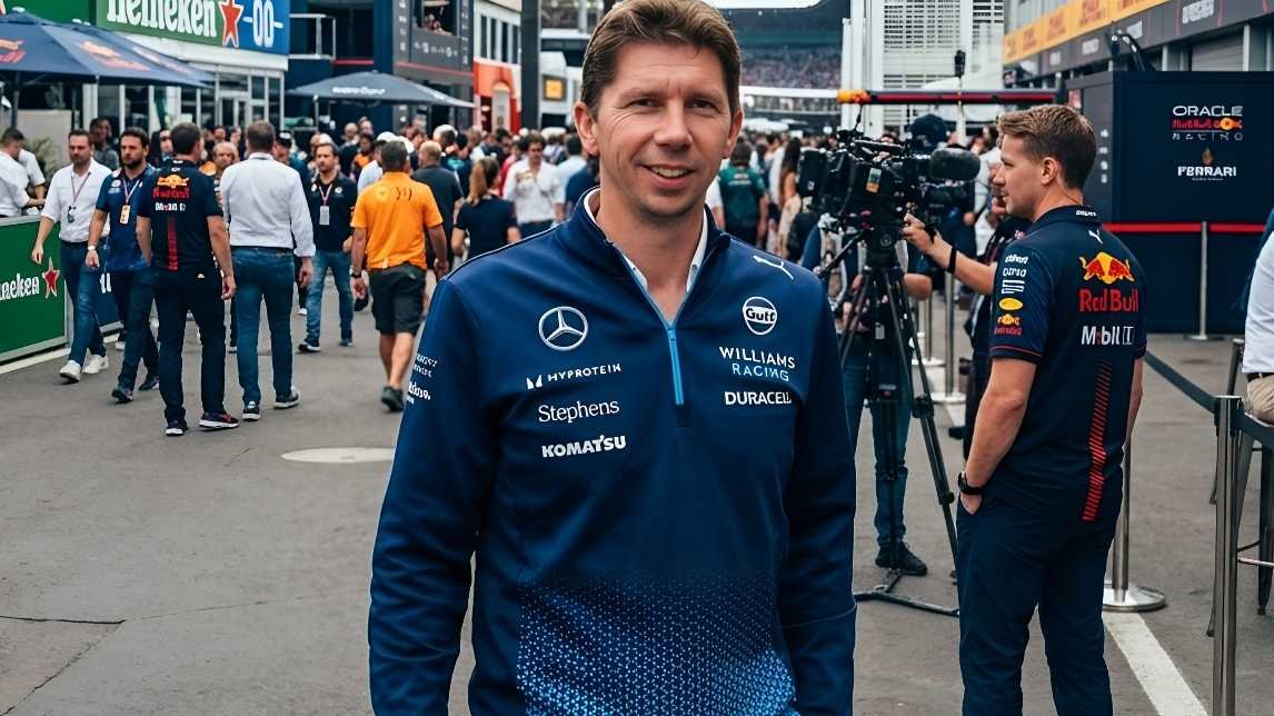 Smiling man wearing Williams Racing team jacket with Mercedes, Gulf, and Duracell logos standing in a crowded Formula 1 paddock with Red Bull and camera crew visible, after FIA and F1 teams reached agreement on 2026 rules