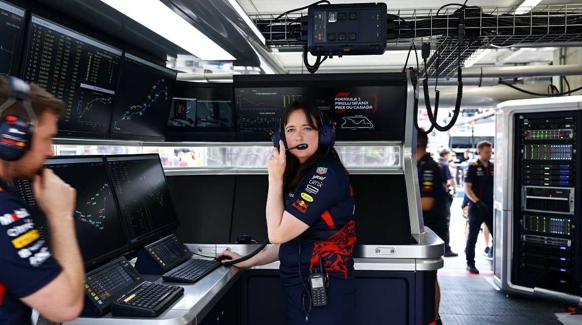 Hannah Schmitz wearing Red Bull team kit and headset, speaking on radio at the strategy desk surrounded by telemetry monitors during a Formula 1 race weekend.