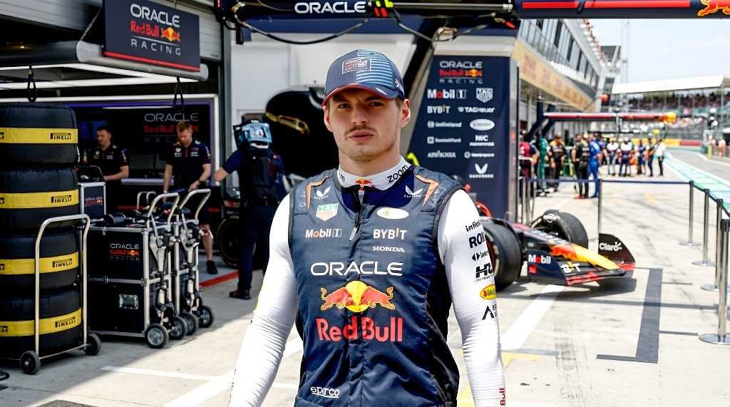 Max Verstappen wearing Red Bull Racing team kit and cap in the F1 paddock, with Oracle Red Bull Racing garage in background
