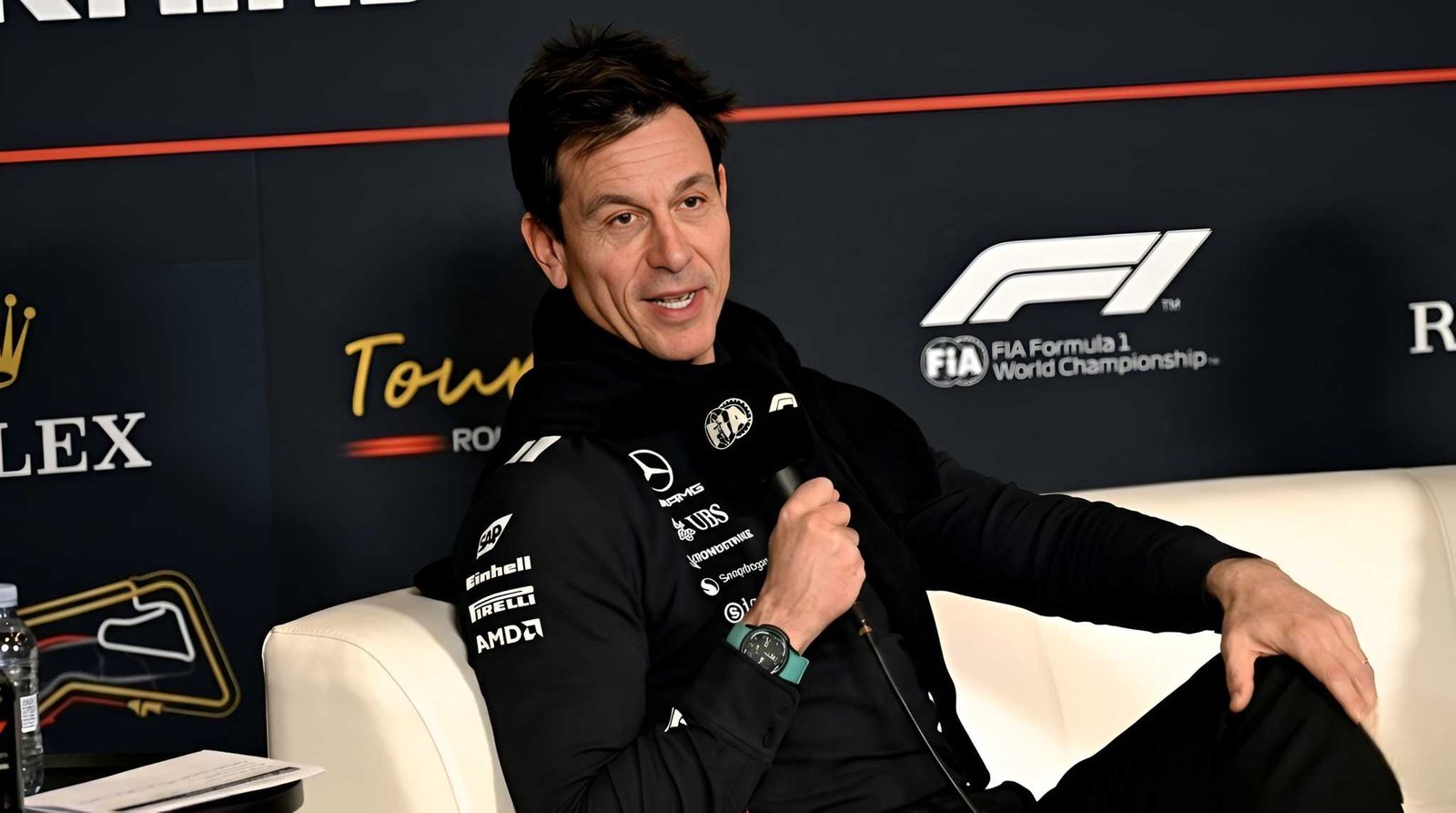 Mercedes F1 team principal Toto Wolff speaking into a microphone at FIA Formula 1 press conference wearing Mercedes team gear with F1 and sponsor logos visible